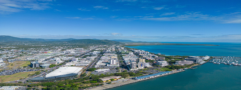 An aerial shot of Cairns on a sunny day with the ocean to the right and mountains in the background.