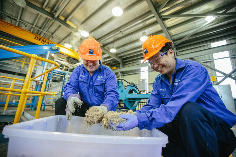 Two men wearing hard hats smiling while sorting recycled material